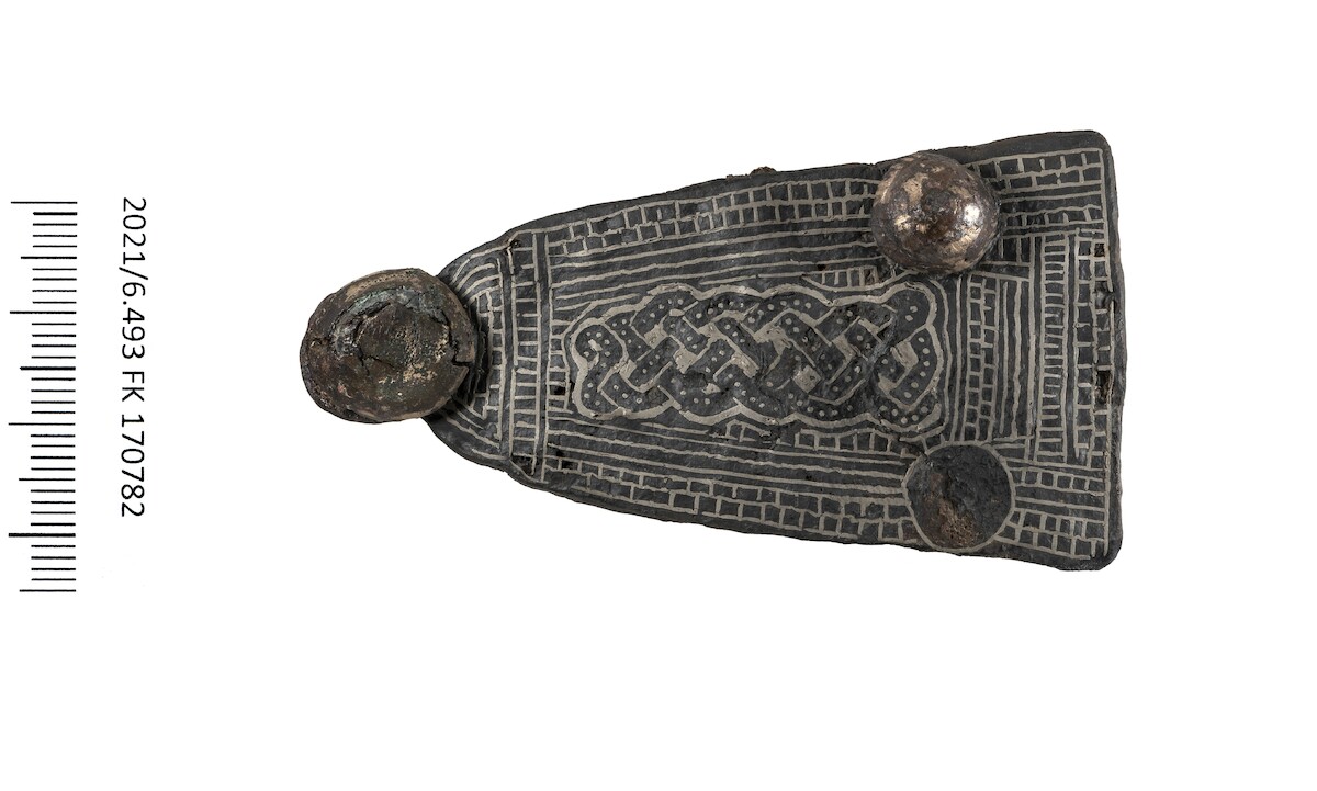 Okucie pasa inkrustowane srebrem odkryte w grobie dziecka (VII w.), Kleinbasel, Szwajcaria. Źródło:  <a href='https://www.archaeologie.bs.ch/ueber-uns/medienmitteilungen/goldene-gewandschliesse.html' rel='noopener'>Archaologische Bodenforschung Basel-Stadt</a>.